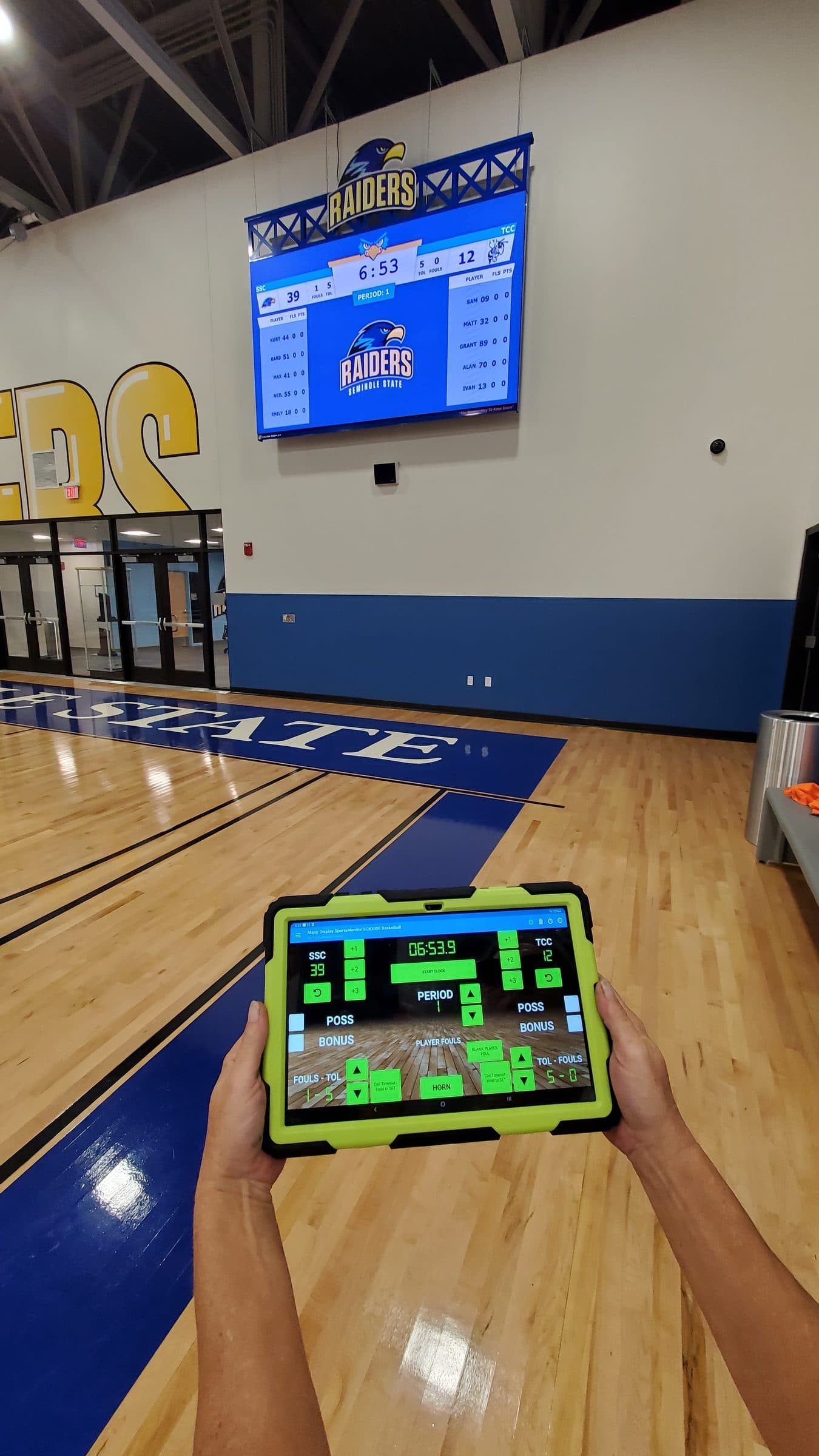 A hand holding the SCB3000 app controlling a Major Display video scoreboard at Seminole State