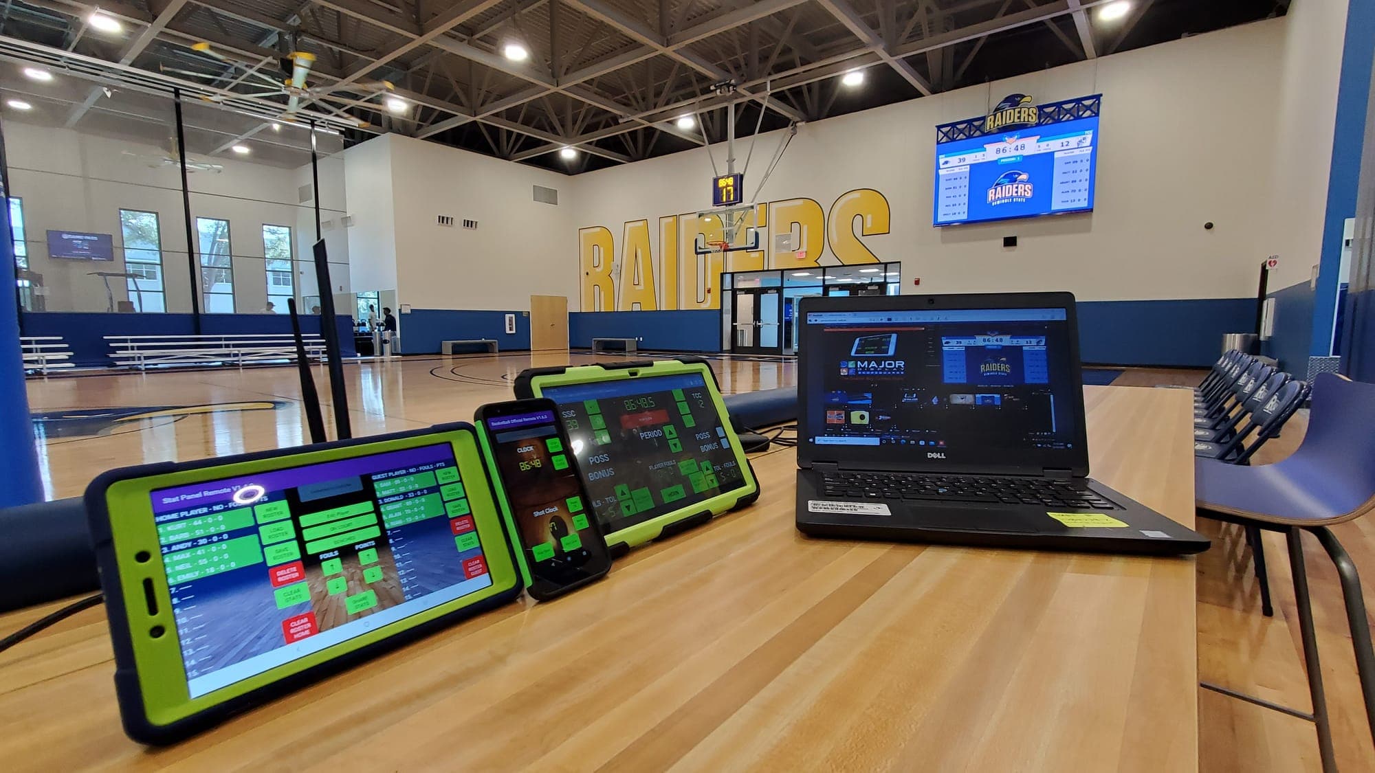 SCB3000 controller tablets and a laptop at the scorer's table in the Seminole State gym, with the video board on the wall behind them