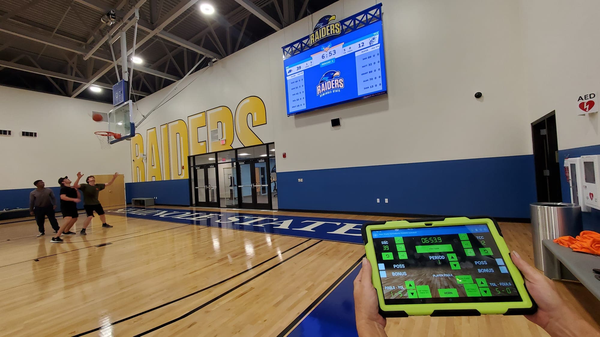 The SCB3000 app on a tablet in hand, running the Seminole State video scoreboard on the gym wall